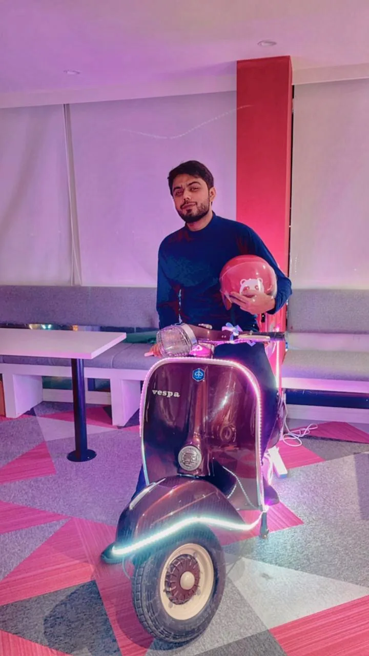 Taimour Tariq sitting on a Vespa and holding a Foodpanda rider helmet at an office event
